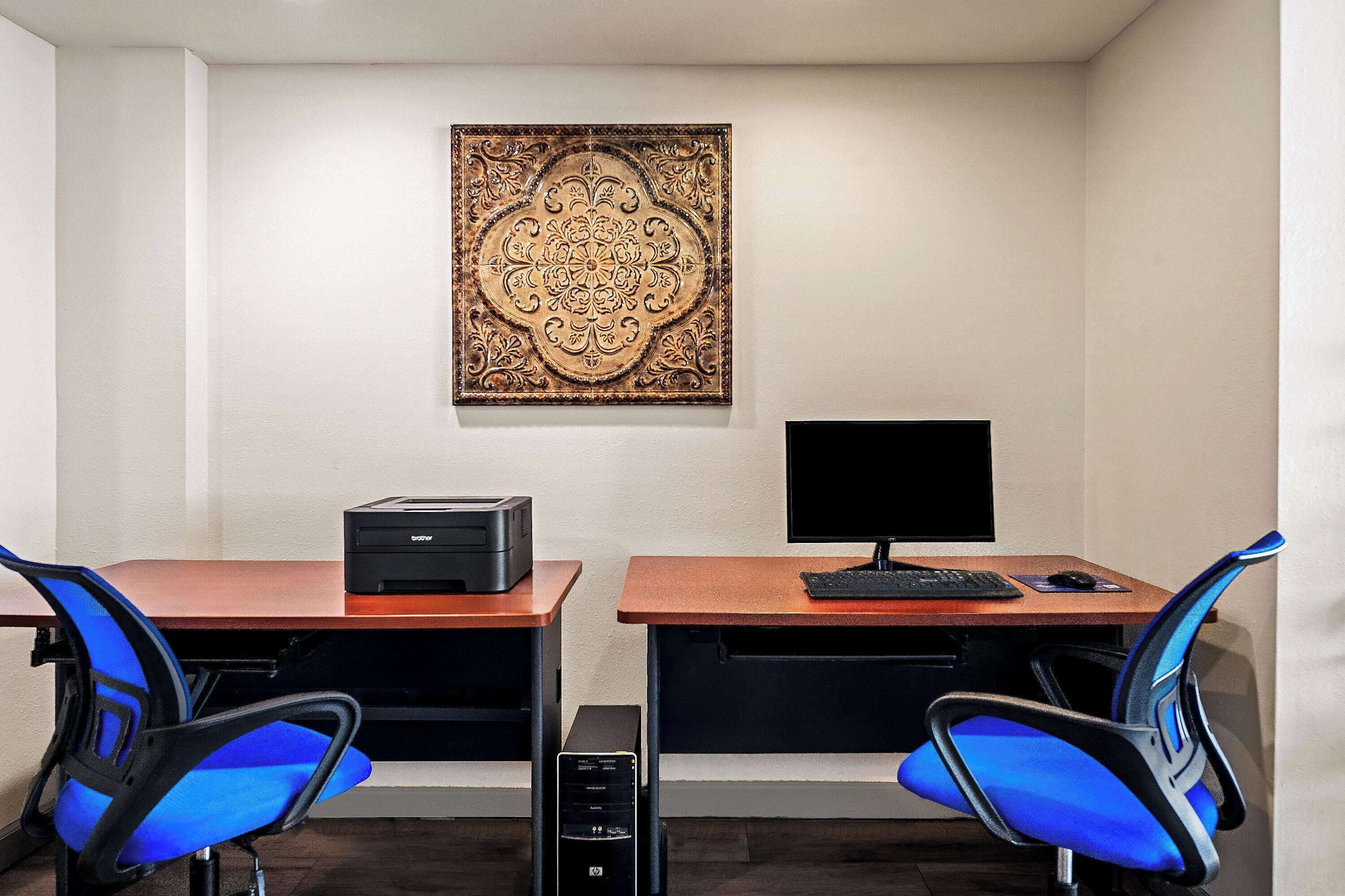 A room with two desks, each with a computer monitor and keyboard, and two blue chairs.