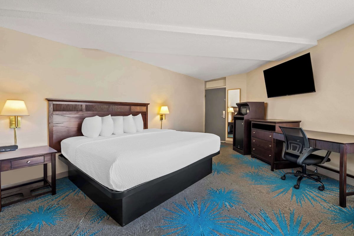 A hotel room with a large bed, a desk, a chair, a TV, and a desk lamp.