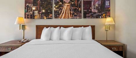Habitación de hotel con una cama grande, dos mesitas de noche con lámparas y un cuadro de un paisaje urbano en la pared.