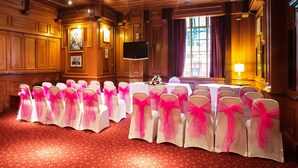 A conference room with rows of white chairs with pink sashes, a large table, and a television. - The Royal Hotel Hull (Hull)