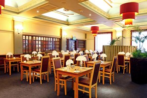 A restaurant with wooden tables and chairs, red hanging lamps, and a large window with blinds. - The Royal Hotel Hull (Hull)