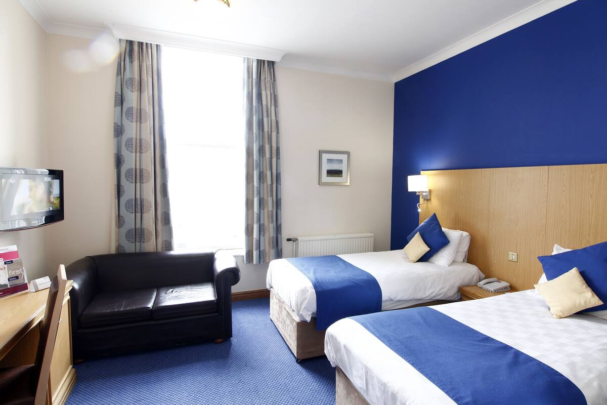 A hotel room with two beds, a sofa, a TV, and a window with curtains.