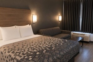 Une chambre d’hôtel avec un grand lit, un canapé, deux lampes fixées au mur, un appareil de climatisation et une fenêtre avec des rideaux.
