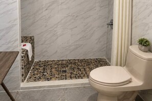 A bathroom with a shower, toilet, and a small table with a towel.