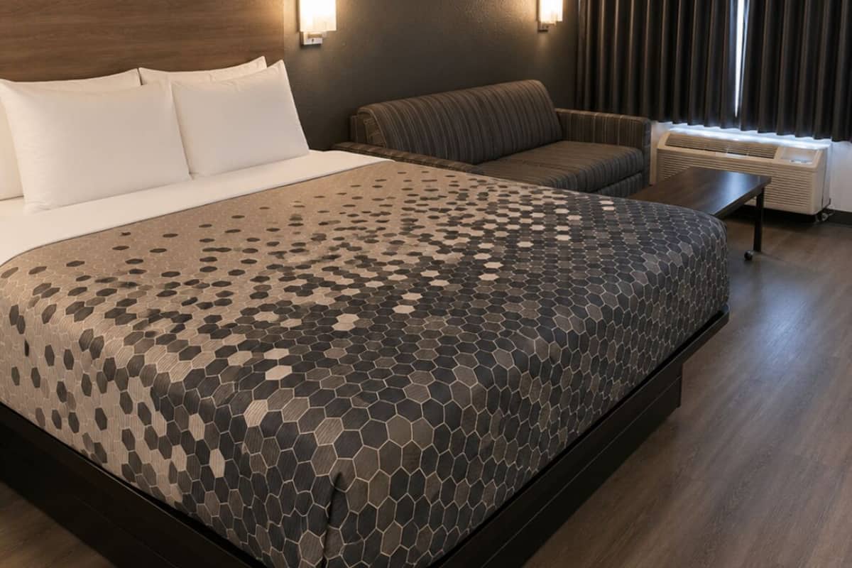 A hotel room with a bed, a sofa, a desk, and a window with curtains.