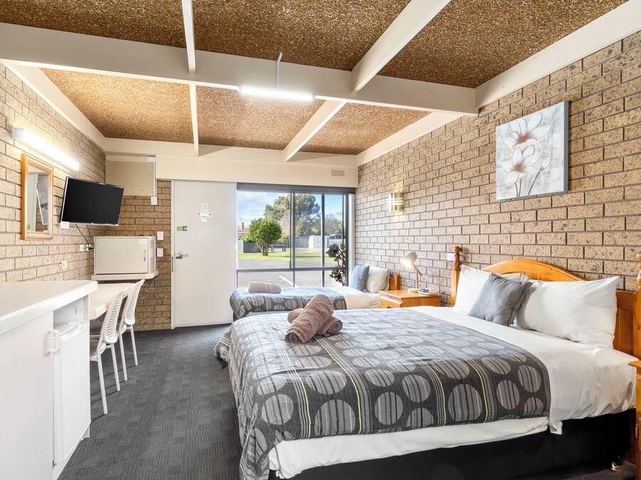 A hotel room with a brick wall, a bed with a patterned bedspread, a desk with a computer, and a television.