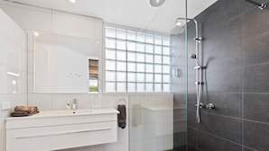 A modern bathroom with a glass shower enclosure, a white vanity with a mirror, and a window providing natural light. - Baronga Motor Inn (Colac)