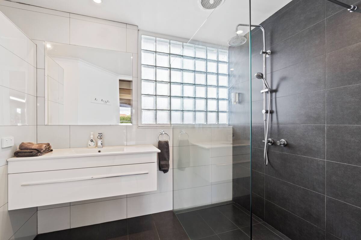 A modern bathroom with a glass shower enclosure, a white vanity with a mirror, and a window providing natural light.
