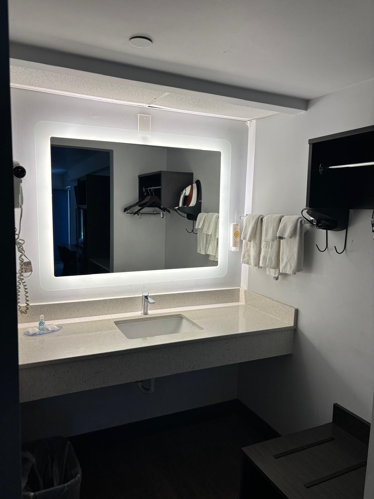 A modern bathroom with a large mirror, a sink, a towel rack, and a hairdryer.