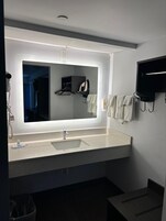Un baño moderno con un espejo grande, un lavabo, un perchero para toallas y un secador de pelo.