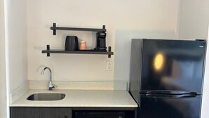 A kitchen with a black refrigerator, a microwave, a sink, and a coffee maker on a shelf. - Clarion Pointe (Dublin)