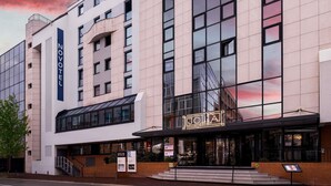Un hotel moderno con un llamativo letrero de 'NOVOTEL', fachada de vidrio y entrada al restaurante 'JOLIA'.