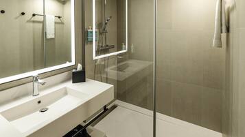 A modern bathroom with a large mirror, a sink, a shower, and a glass-enclosed shower area.