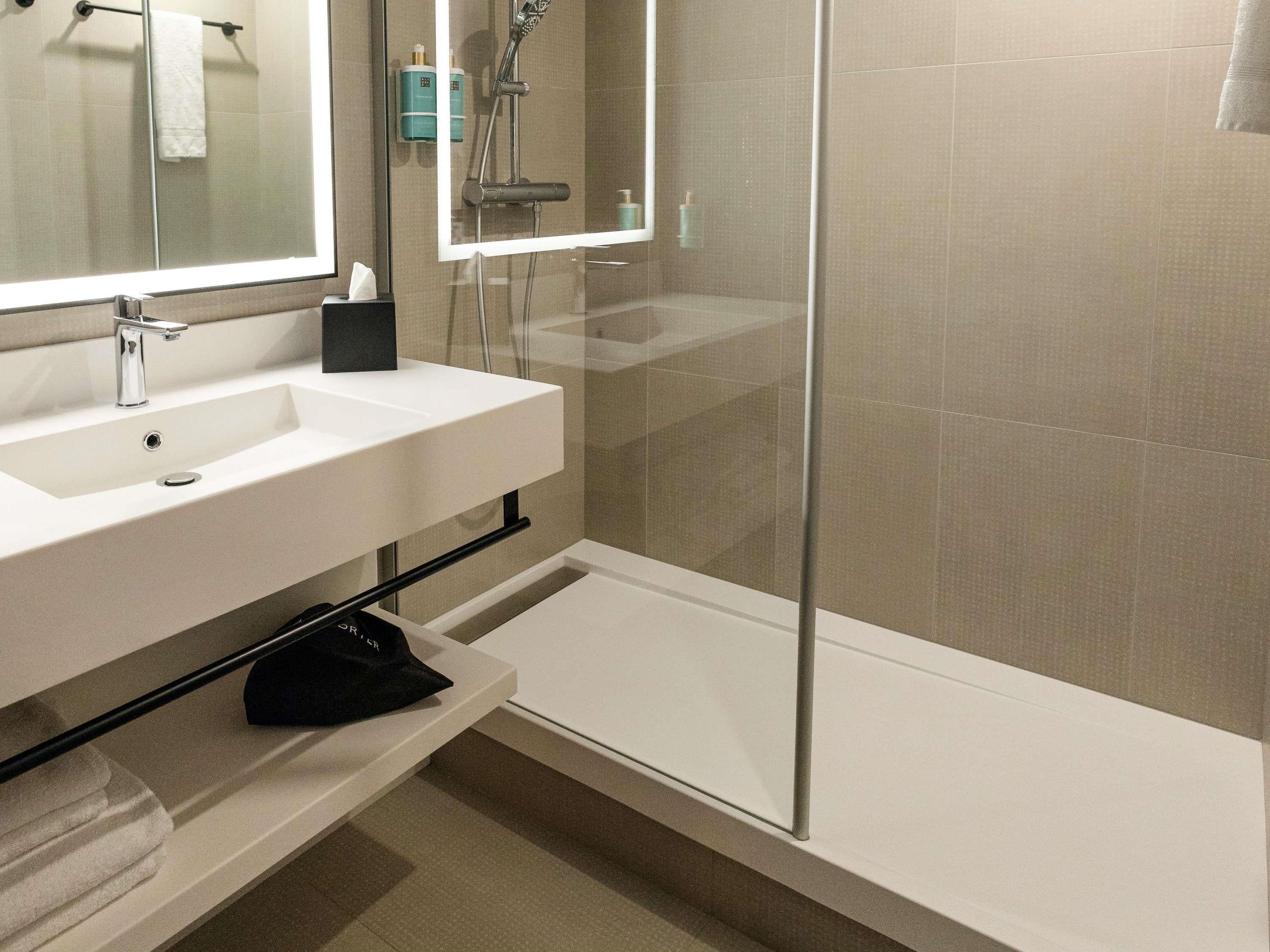 Ein modernes Badezimmer mit einem weißen Waschbecken, einem Spiegel, einem Handtuchhalter und einer Duschkabine.