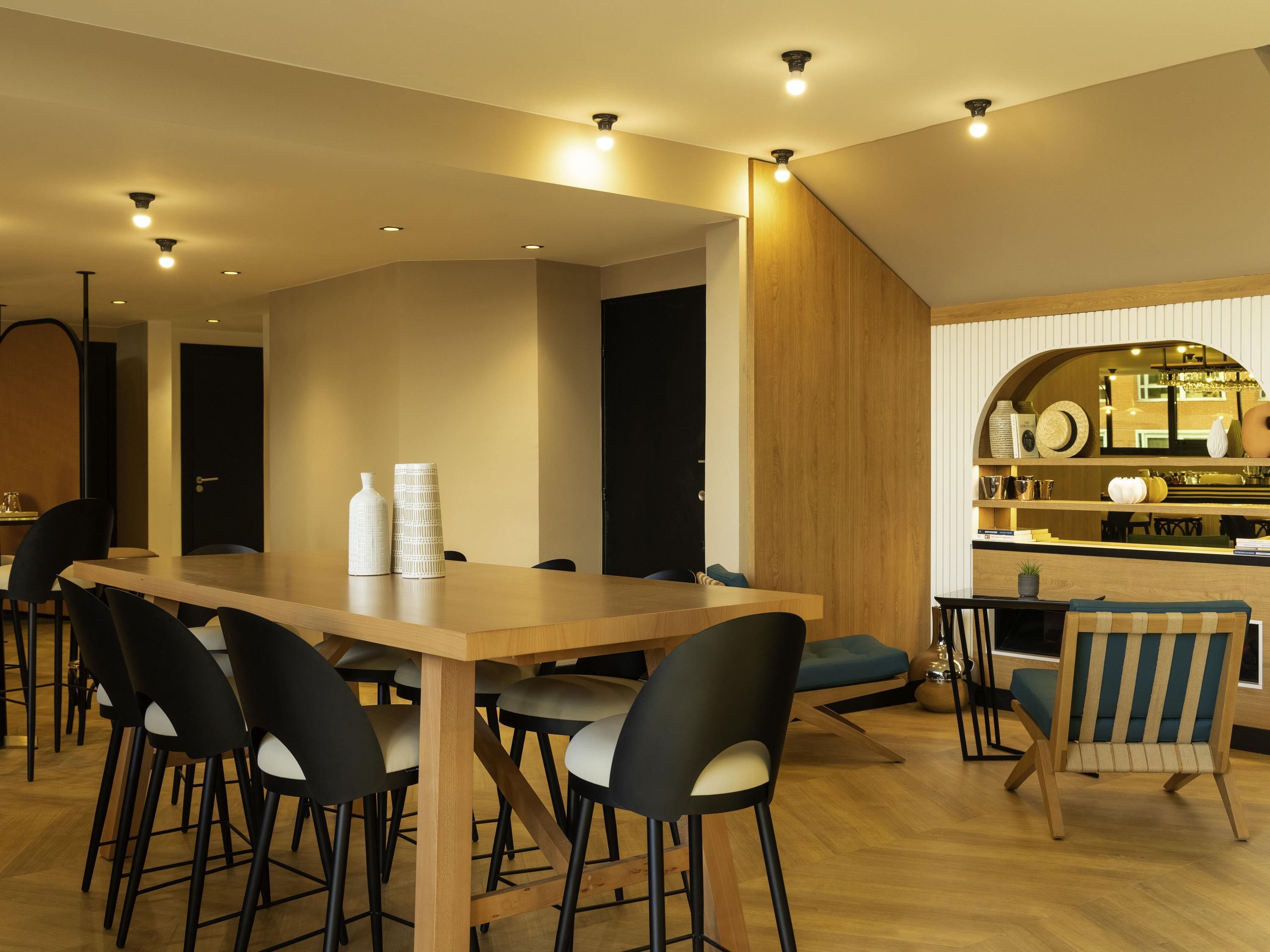 A modern dining area with a wooden table, black chairs, and a bar counter with various items.