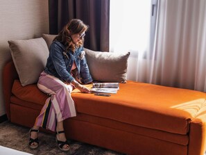 A person sitting on a sofa with a magazine, a remote control, and a smartphone on it. - Novotel Paris Suresnes Longchamp (Suresnes)