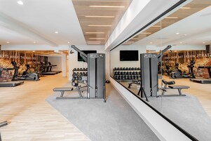 Una palestra con attrezzature per esercizi, una TV a muro e uno specchio che riflette l'ambiente.