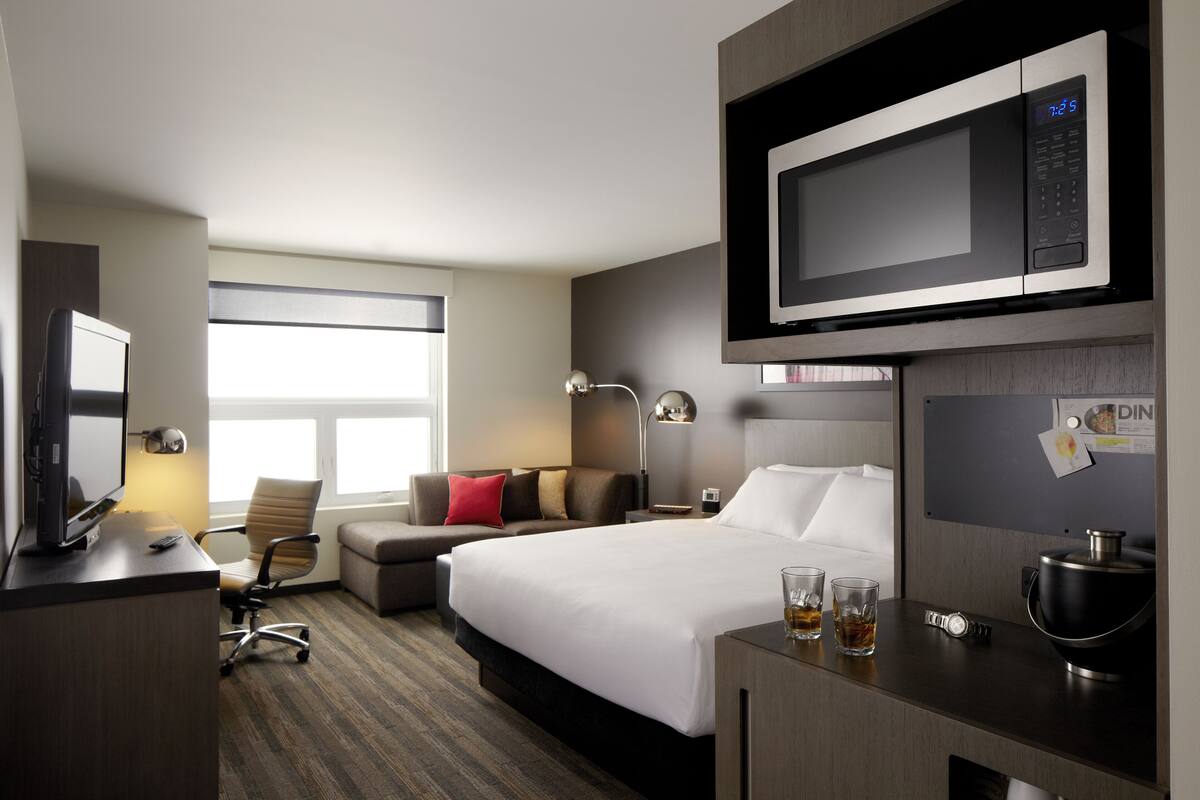 A hotel room with a bed, a desk with a computer, a microwave, a coffee maker, and a window with a view.