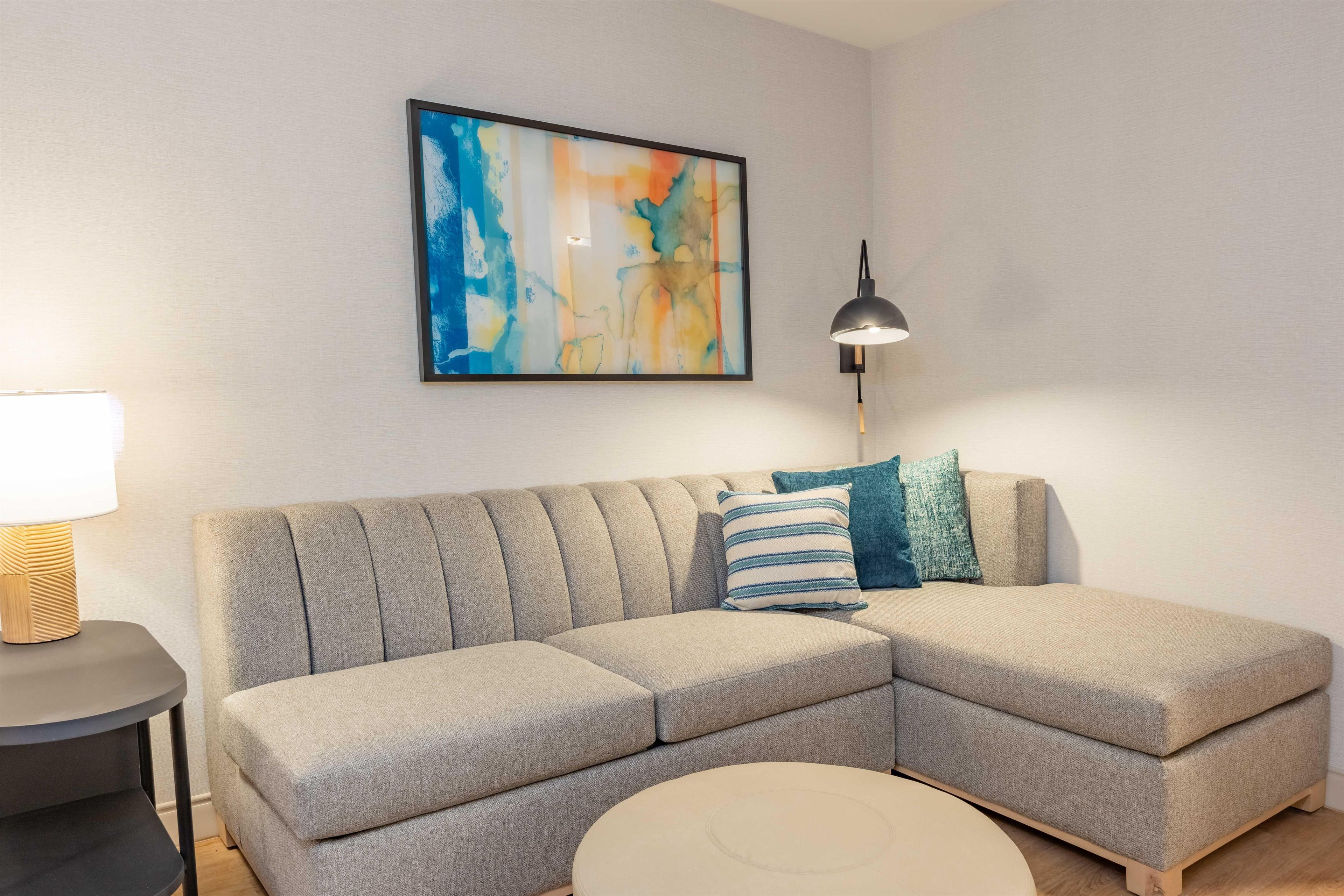 Uma sala de estar moderna com um sofá modular, uma mesa de centro redonda, um abajur e uma pintura abstrata emoldurada na parede.