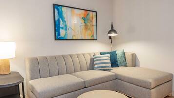 Uma sala de estar moderna com um sofá modular, uma mesa de centro redonda, um abajur e uma pintura abstrata emoldurada na parede.