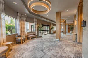 Un'ampia hall dall'arredamento moderno, con un'area relax con divani e poltrone, un'ampia finestra con vista sull'esterno e un originale lampadario circolare.