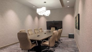 A conference room with a long table, six chairs, a flat-screen TV, and a patterned carpet.