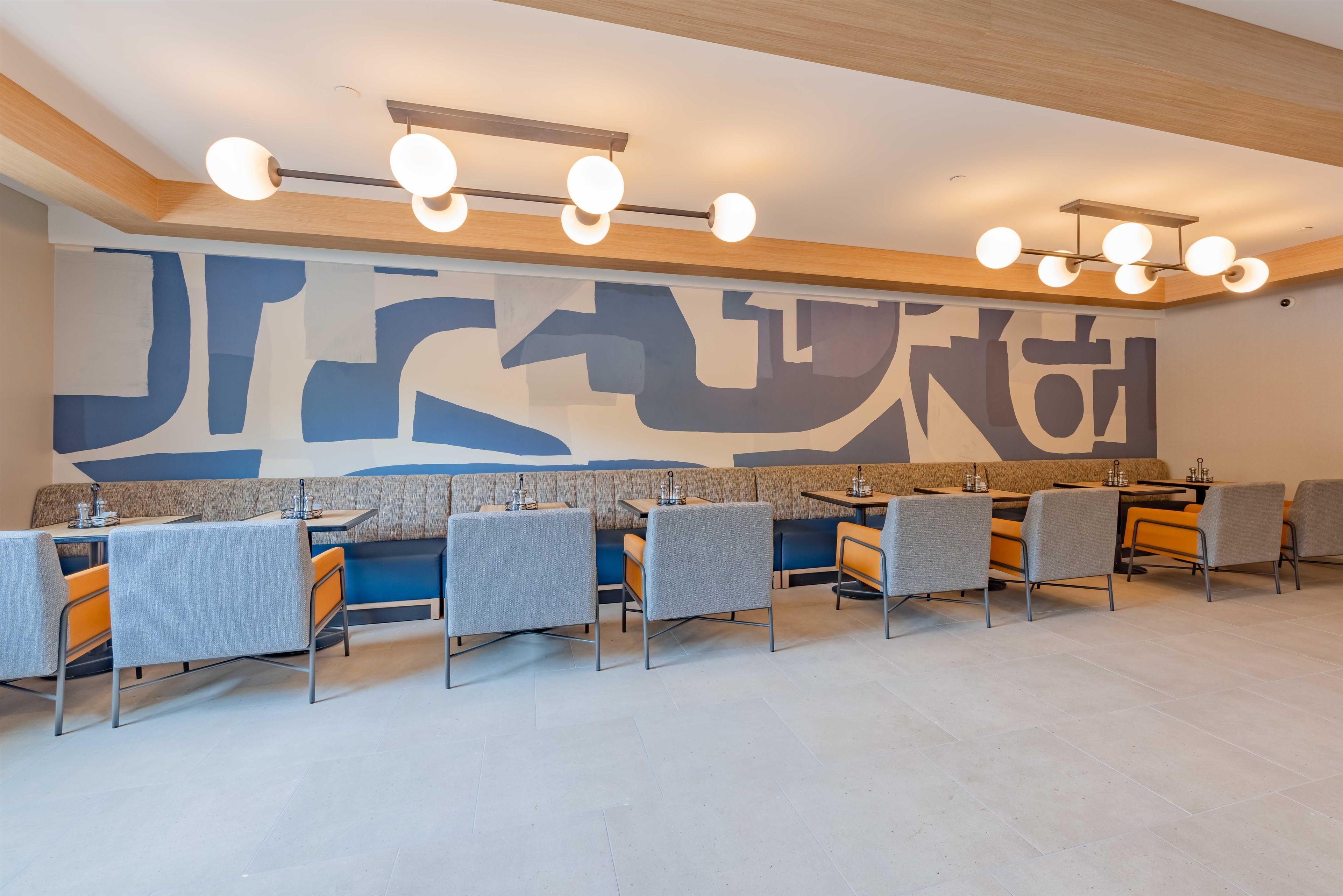 A modern dining area with a large abstract mural, multiple tables and chairs, and a ceiling light fixture.