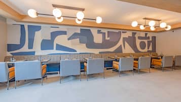 A modern dining area with a large abstract mural, multiple tables and chairs, and a ceiling light fixture.