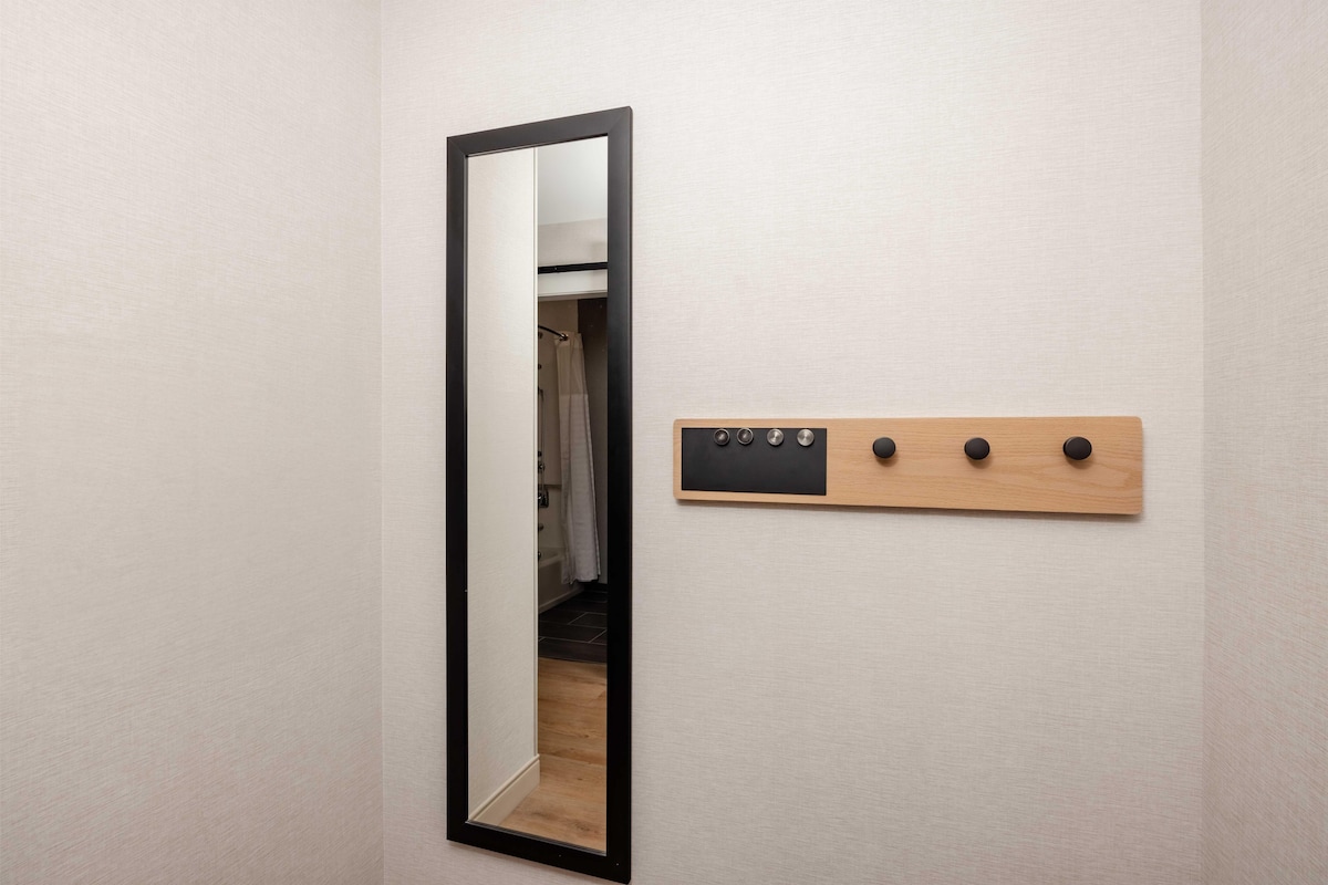 A mirror with a black frame and a wooden coat rack with hooks.