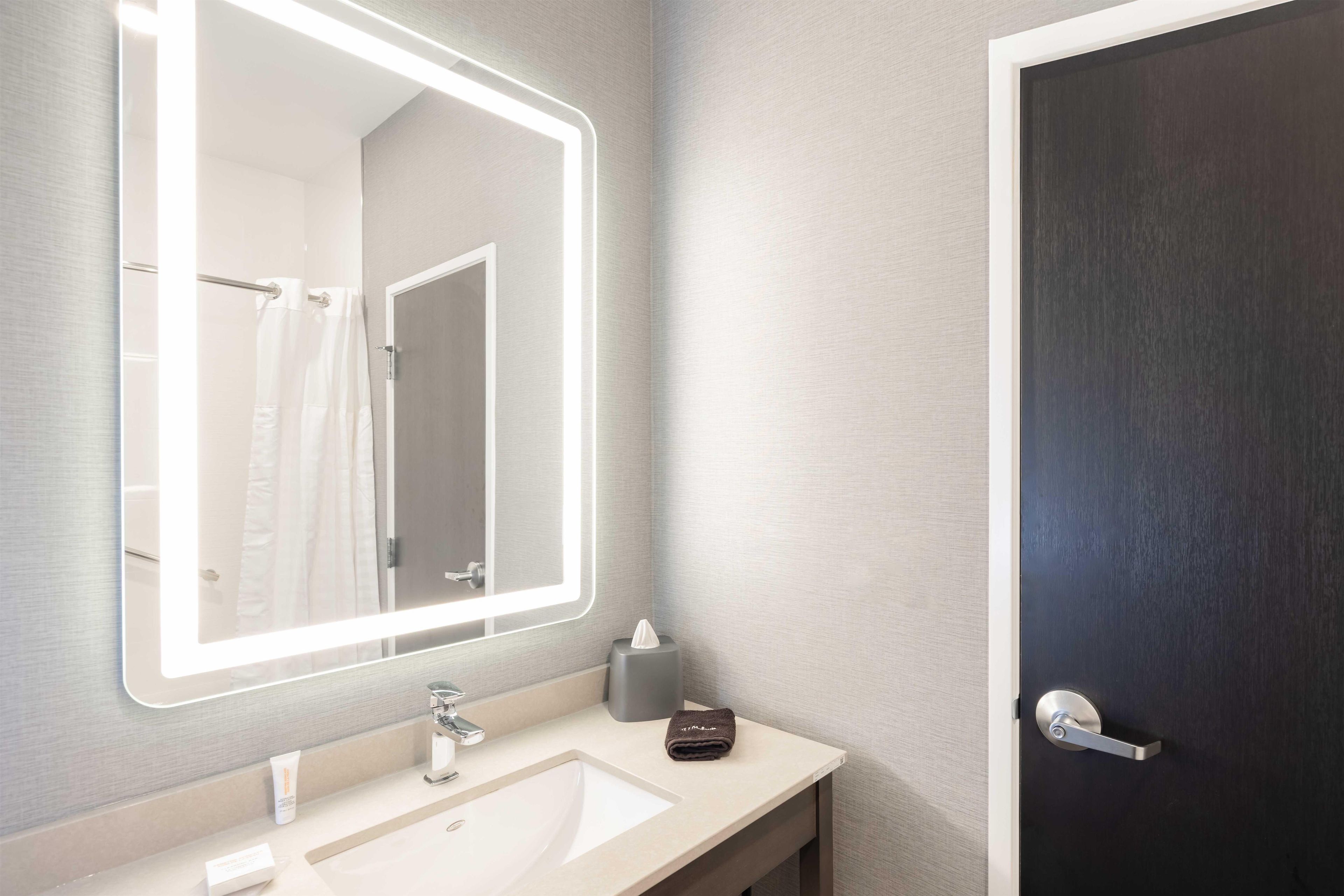 A bathroom with a large mirror, a sink, a towel, and a door.