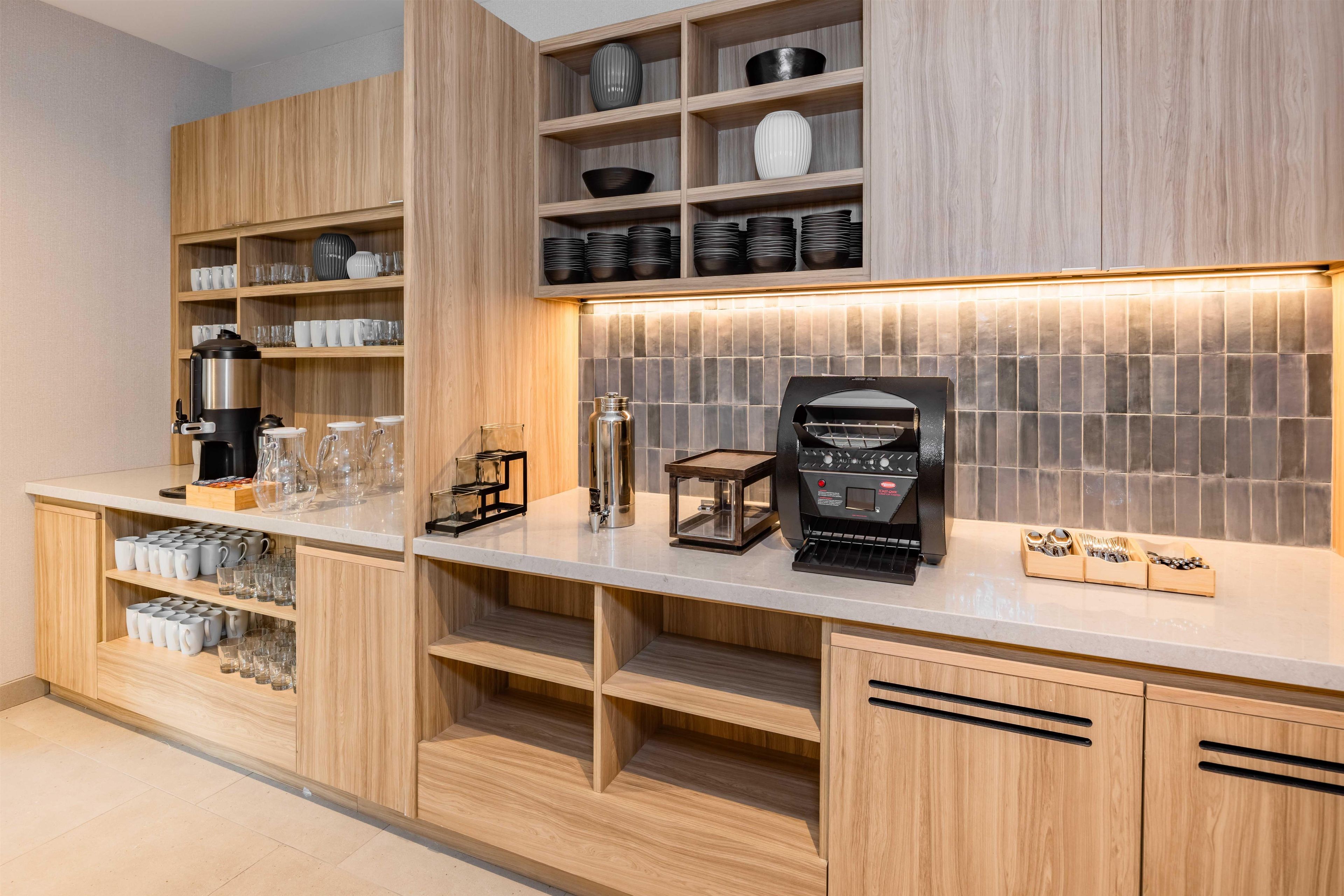 A modern kitchen with wooden cabinetry, a coffee station, and a tiled backsplash.