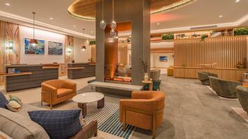 A modern hotel lobby with a reception desk, seating area, and a fireplace.