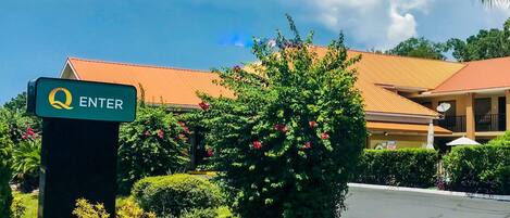 Entrada de hotel com um letreiro verde 'ENTER', rodeada por vegetação exuberante e um edifício com telhado vermelho.
