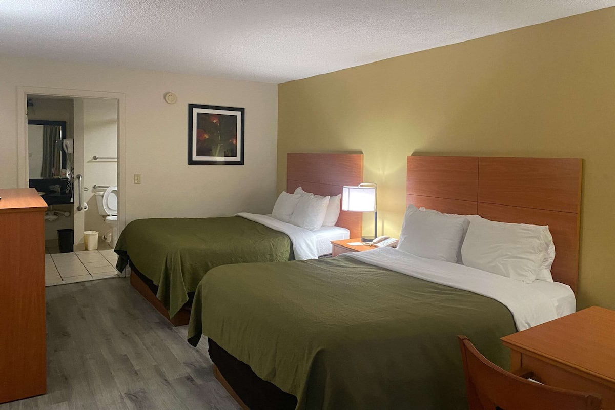 A hotel room with two beds, a desk, a chair, a bedside table, a lamp, and a framed picture on the wall.