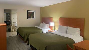 A hotel room with two beds, a desk, a chair, a bedside table, a lamp, and a framed picture on the wall.