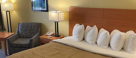 A hotel room with a large bed, a chair, a nightstand with a lamp, and a framed picture on the wall.