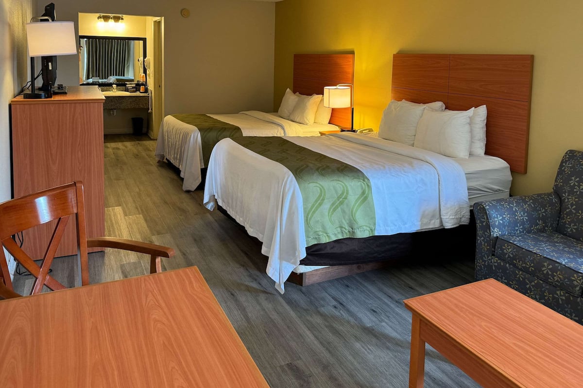A hotel room with two beds, a desk, a chair, and a sofa.
