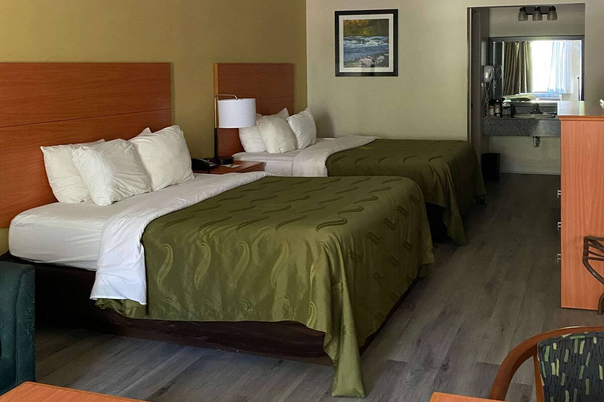 A hotel room with two beds, a desk, a chair, a mirror, and a window with a view of a river.