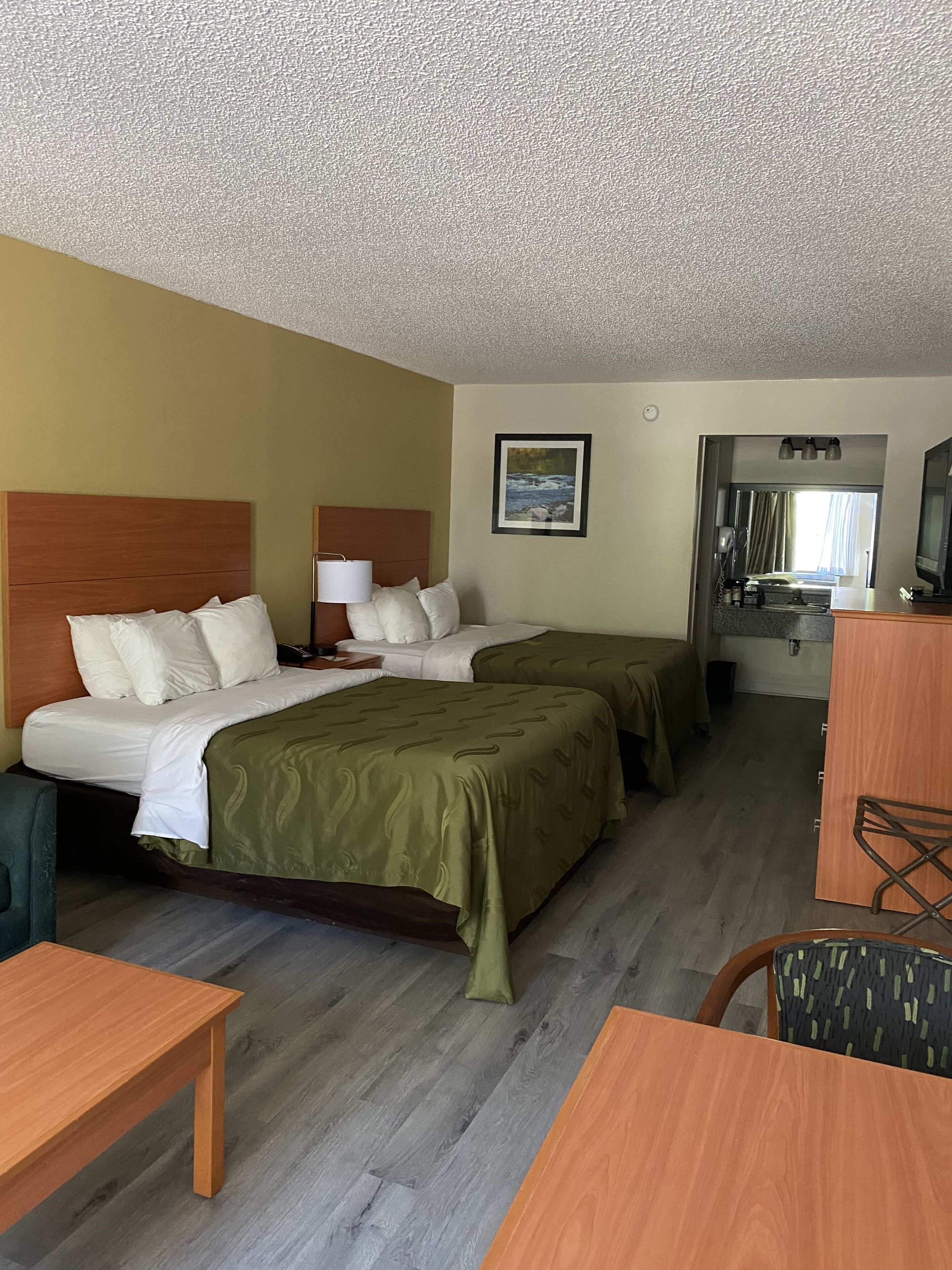 A hotel room with two beds, a desk, a chair, a TV, and a bathroom visible through an open door.