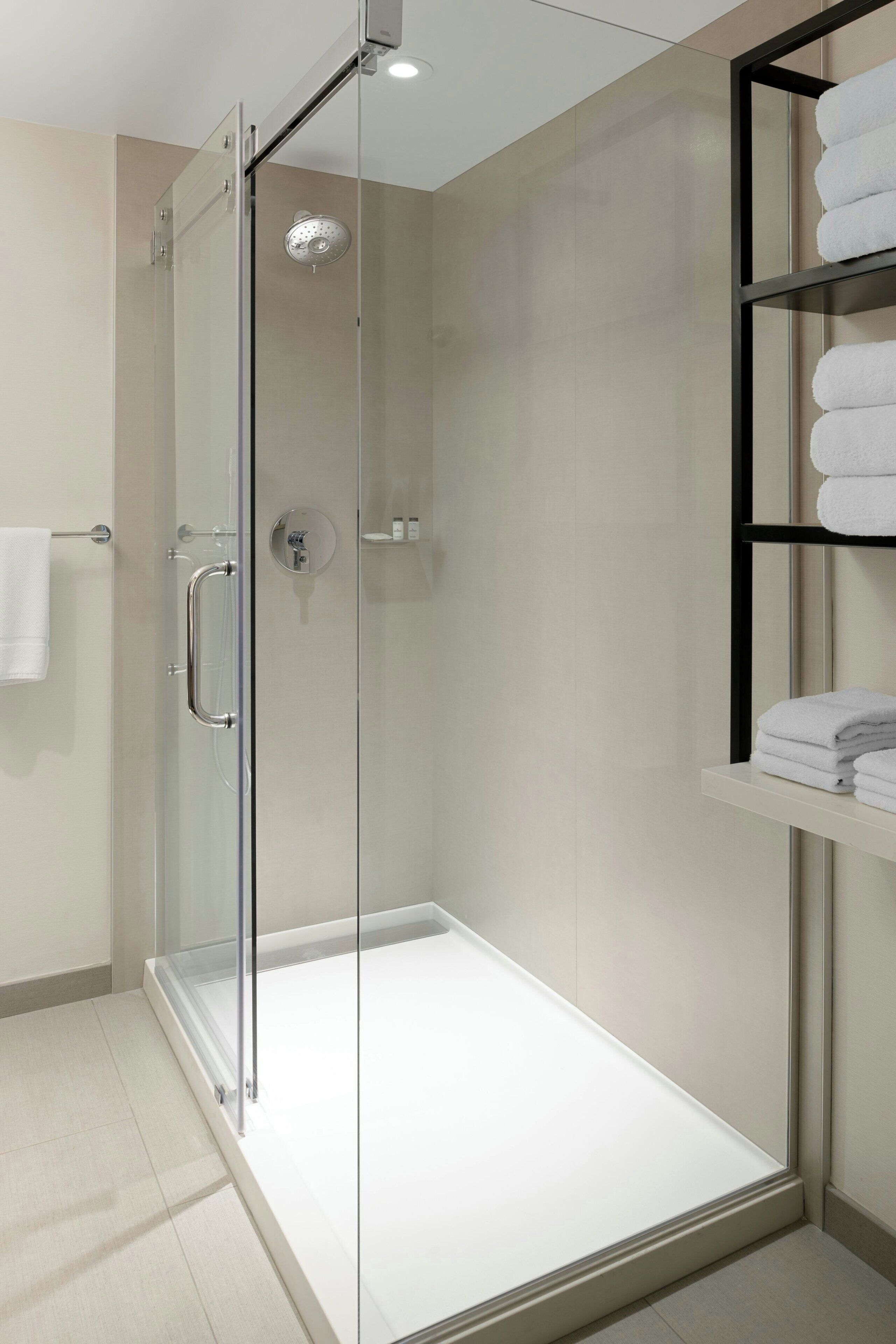 A modern bathroom with a glass-enclosed shower, a white towel rack, and a shelf with folded towels.