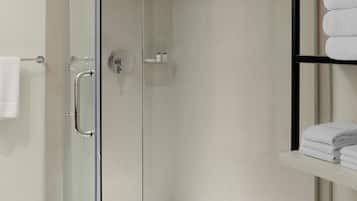 A modern bathroom with a glass-enclosed shower, a white towel rack, and a shelf with folded towels.