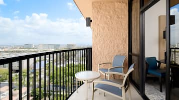 Un balcón con mesa y sillas, vista panorámica de la ciudad y un ventanal grande.