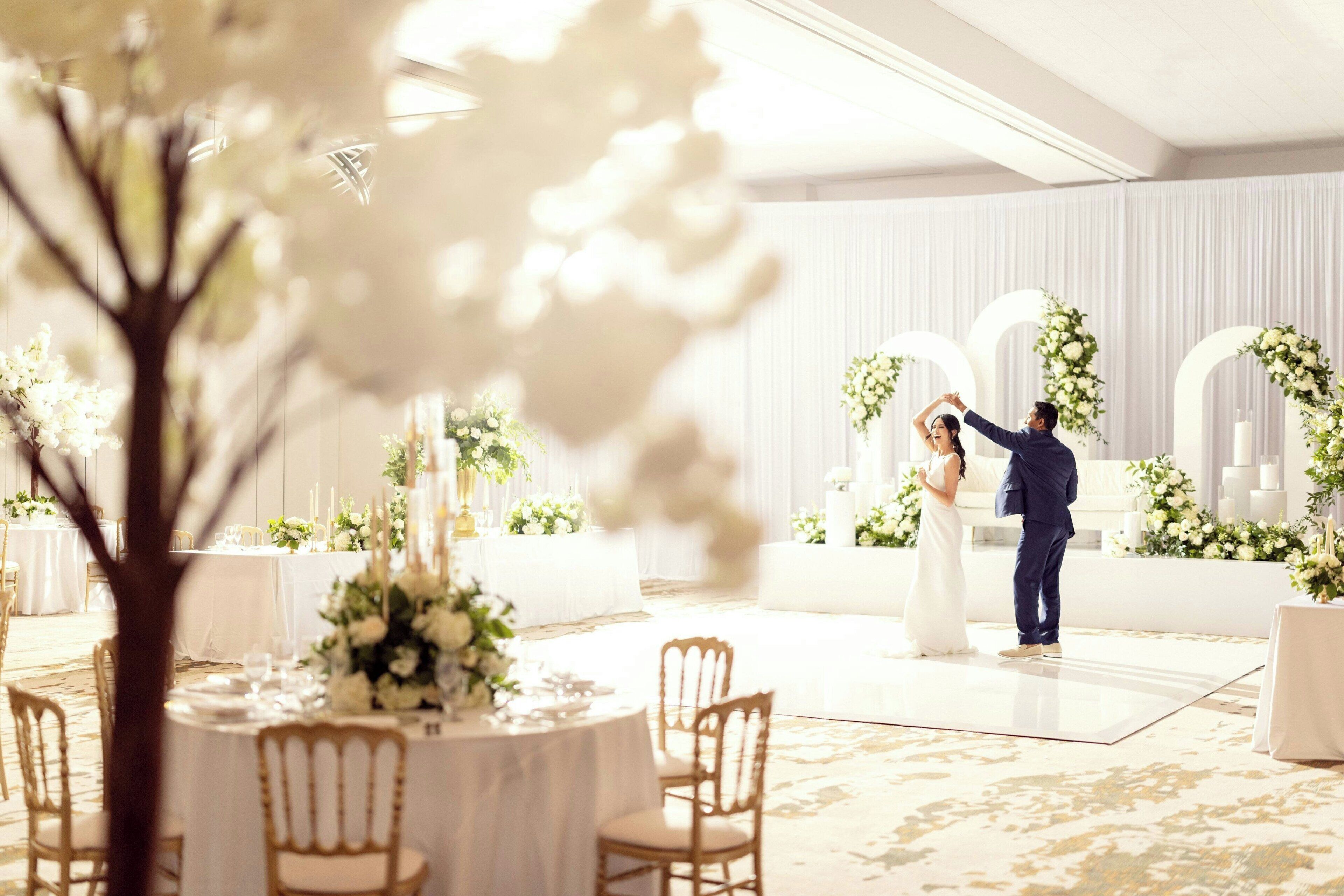 A wedding reception with round tables, white floral arrangements, and a dance floor.