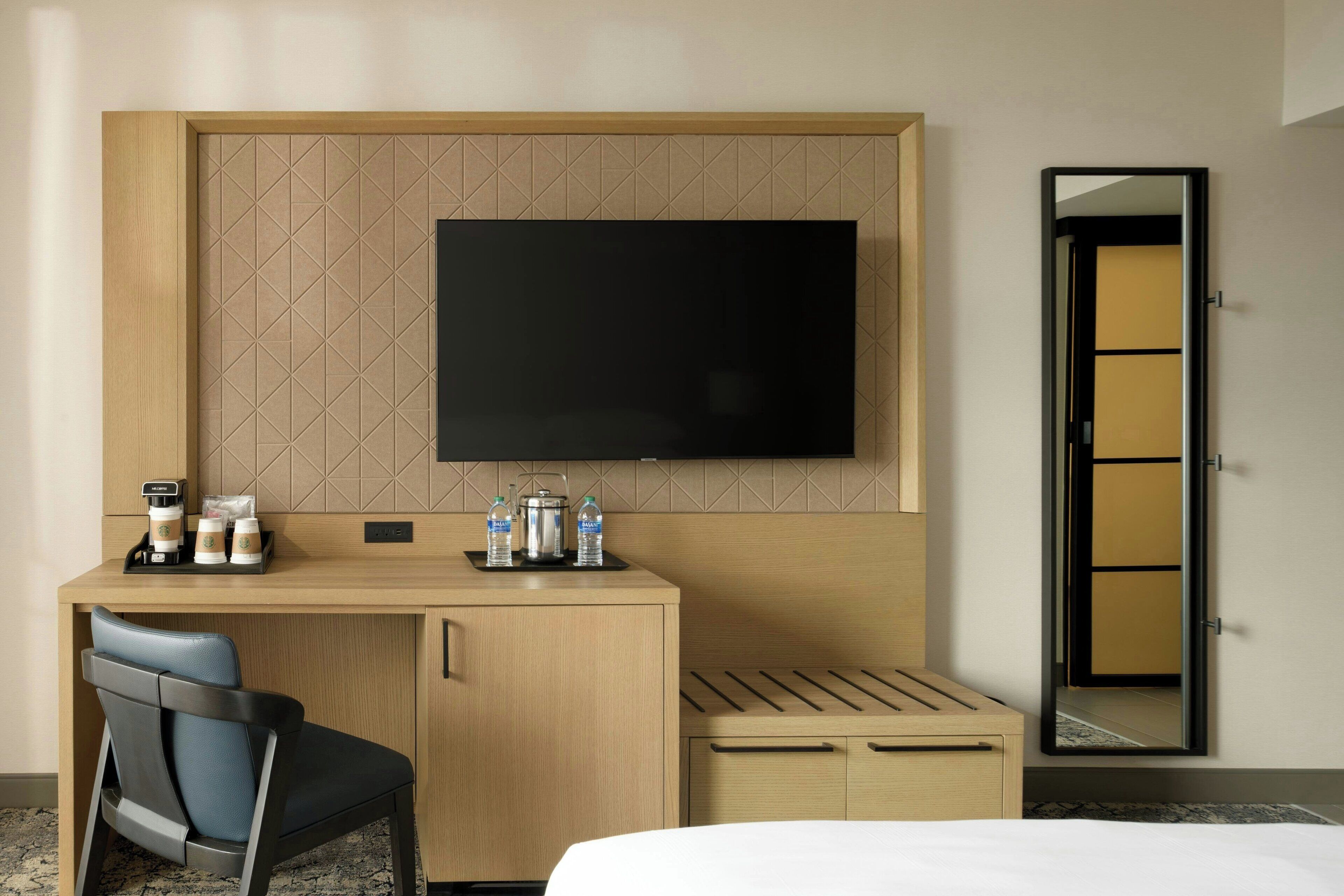 Une chambre d’hôtel équipée d’un bureau en bois, d’un téléviseur à écran plat, d’une chaise, d’un lit et d’un miroir.