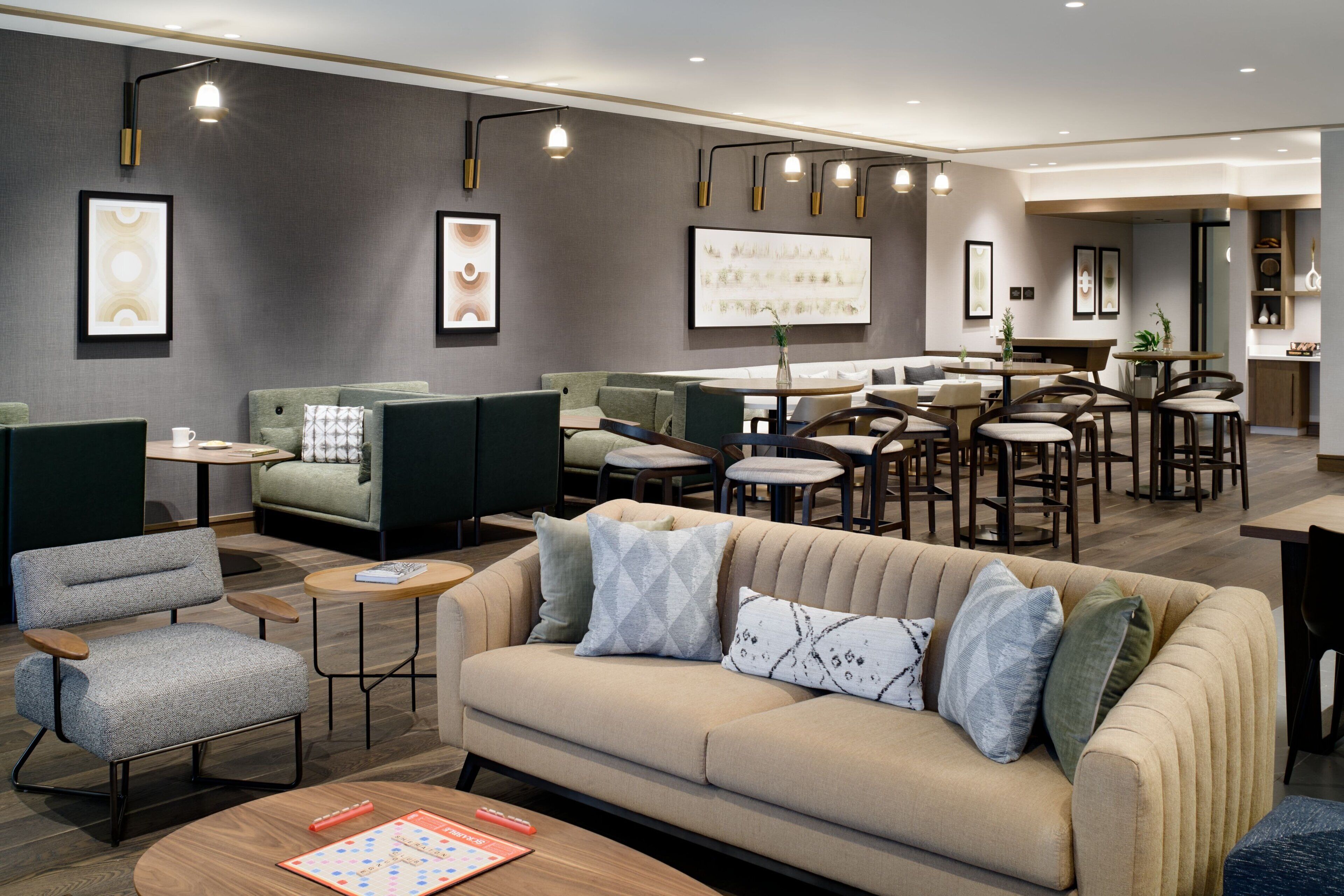 A modern lounge area with sofas, chairs, and tables, featuring artwork on the walls and pendant lighting.