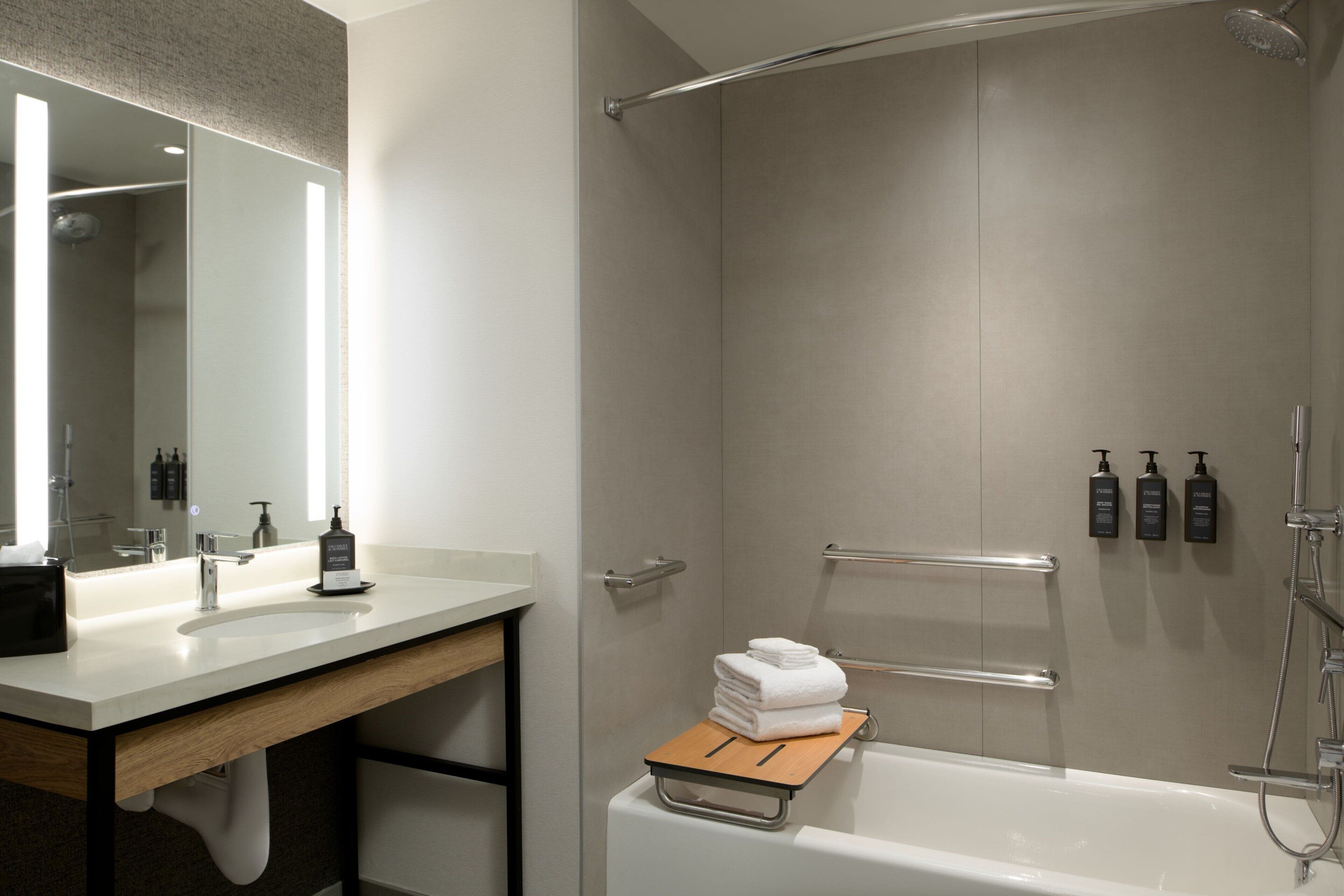 A modern bathroom with a white sink, mirror, and bathtub. There are toiletries on the wall and a towel rack.