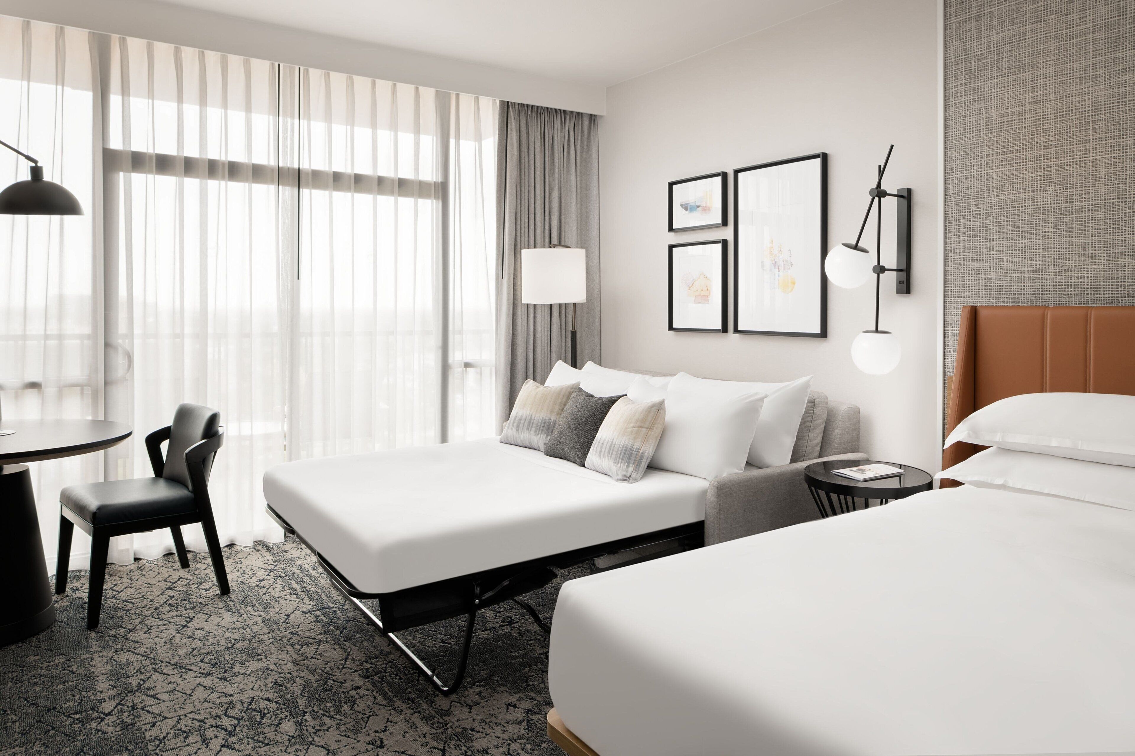 Une chambre d’hôtel avec deux lits, un bureau, une chaise, une lampe et des tableaux encadrés au mur.