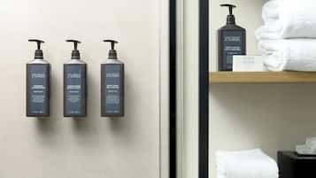 Three bottles of Gilchrist & Soames body wash and conditioner on a wall, a folded white towel on a shelf, and a Gilchrist & Soames skincare bar.