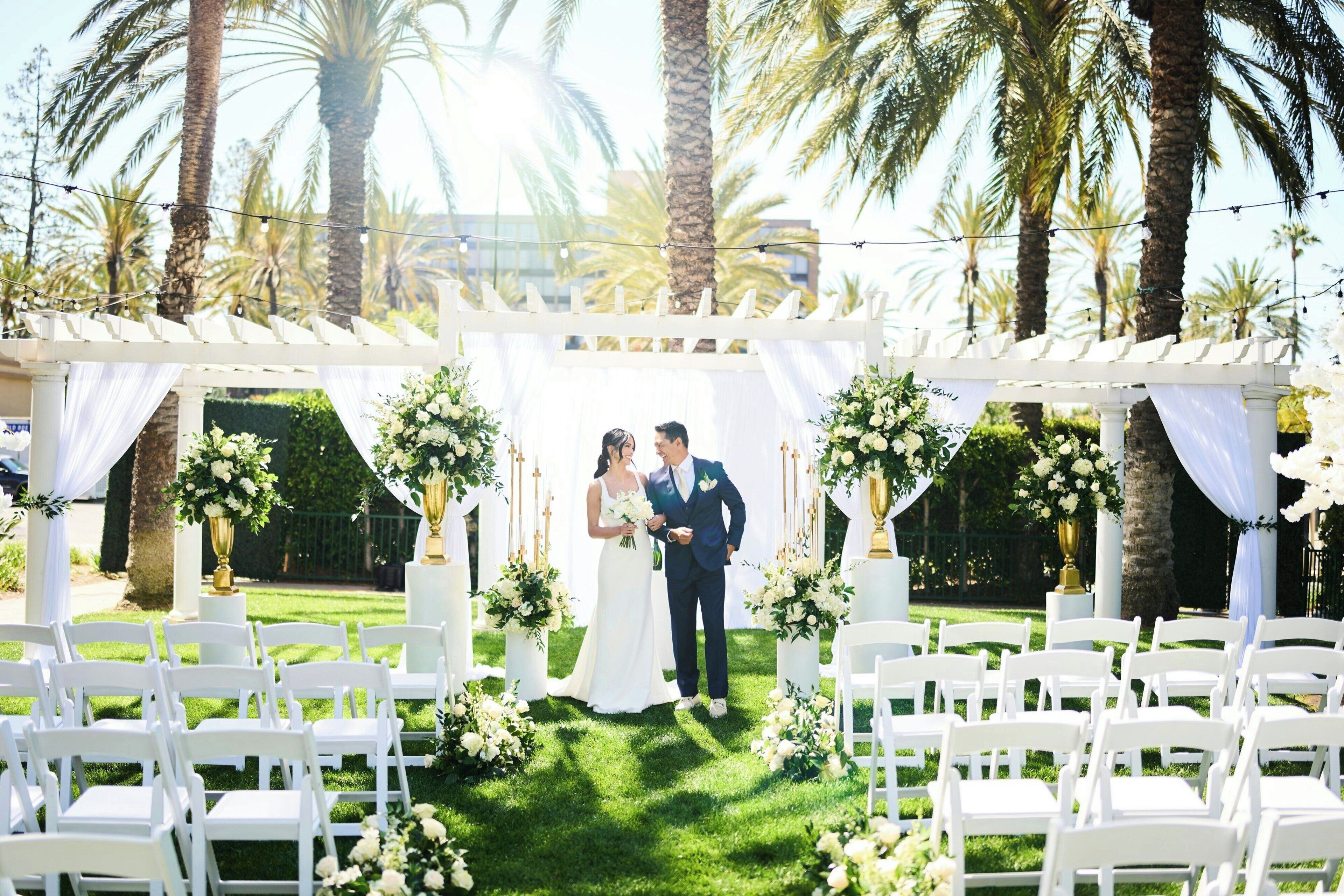 Une cérémonie de mariage avec des chaises blanches et une arche blanche décorée de fleurs.