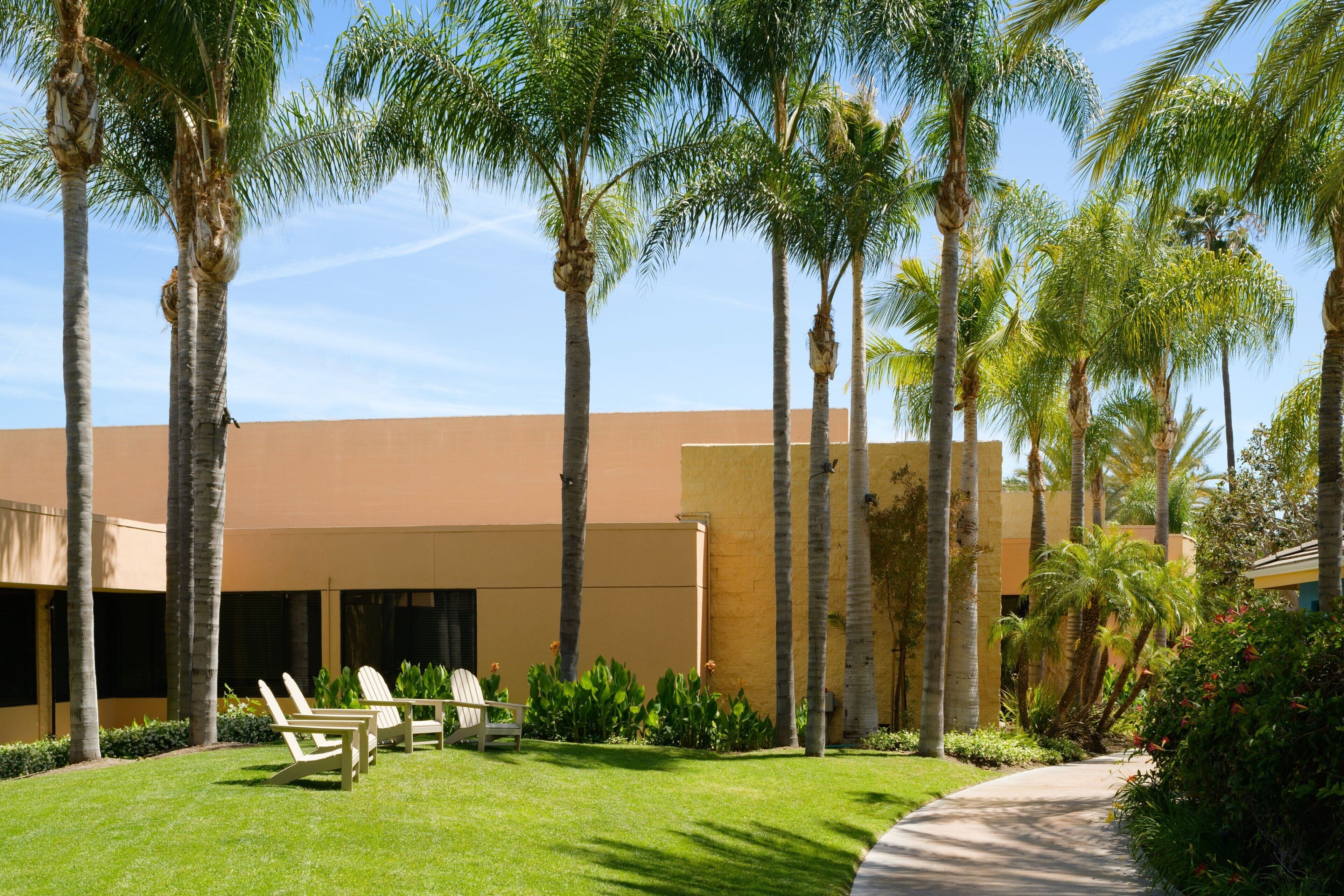 A building with a flat roof, surrounded by palm trees and a well-maintained lawn.